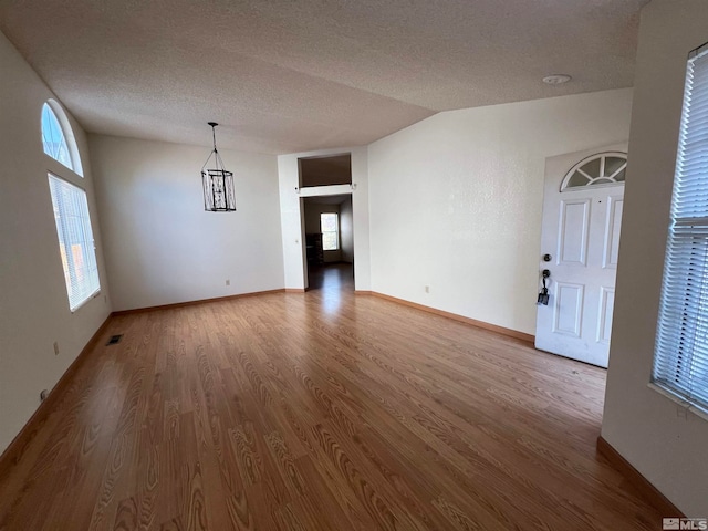 unfurnished room featuring hardwood / wood-style floors, a textured ceiling, an inviting chandelier, and vaulted ceiling