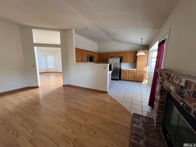 unfurnished living room featuring a brick fireplace, light hardwood / wood-style floors, a textured ceiling, and vaulted ceiling