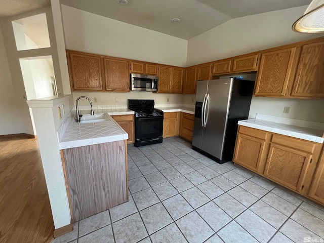 kitchen featuring appliances with stainless steel finishes, light tile patterned floors, sink, tile counters, and vaulted ceiling