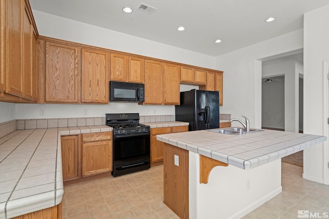 kitchen featuring sink, black appliances, a kitchen breakfast bar, a kitchen island with sink, and tile counters