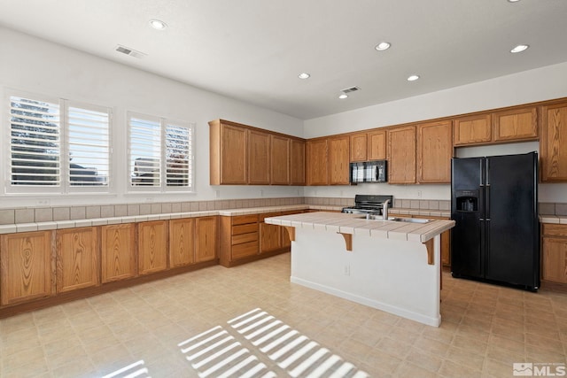 kitchen featuring tile counters, black appliances, a breakfast bar area, and a kitchen island