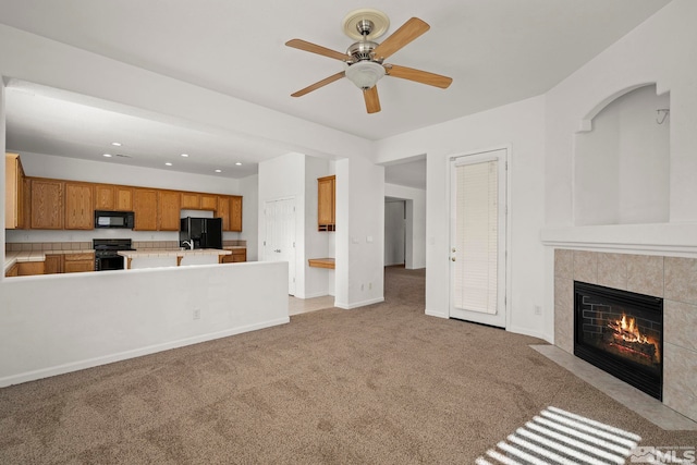 unfurnished living room featuring ceiling fan, a tiled fireplace, and light carpet