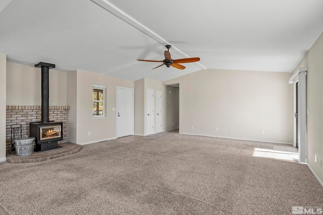 unfurnished living room with a wood stove, carpet floors, ceiling fan, and vaulted ceiling