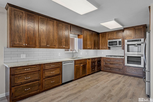 kitchen with stainless steel appliances, light hardwood / wood-style floors, sink, backsplash, and light stone countertops