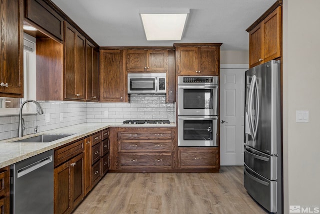 kitchen with stainless steel appliances, sink, light stone countertops, backsplash, and light hardwood / wood-style flooring