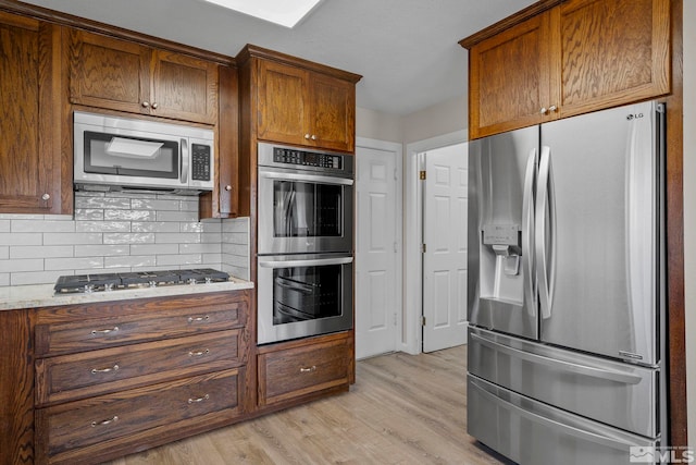 kitchen featuring light wood-type flooring, stainless steel appliances, backsplash, and light stone countertops