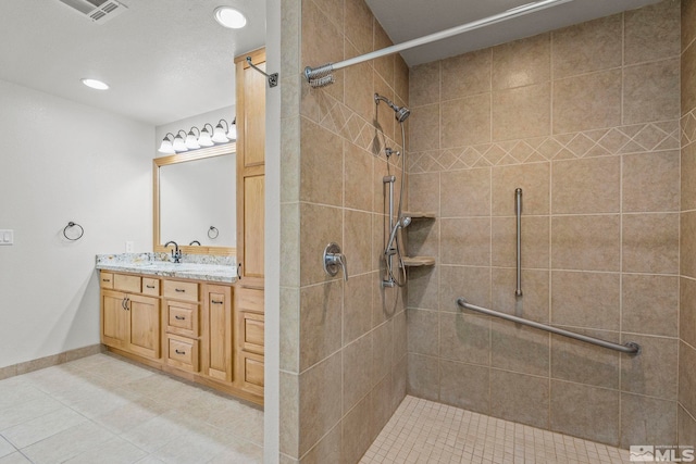 bathroom with tile patterned flooring, vanity, and a tile shower