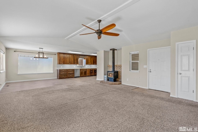 unfurnished living room with ceiling fan, a wood stove, lofted ceiling with beams, and carpet