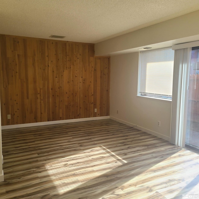 spare room featuring wood-type flooring, a textured ceiling, and wooden walls