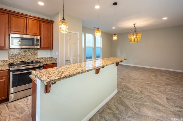 kitchen with a kitchen bar, stainless steel appliances, decorative light fixtures, and light stone countertops