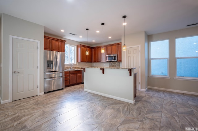 kitchen featuring a kitchen bar, a kitchen island, light stone countertops, pendant lighting, and appliances with stainless steel finishes