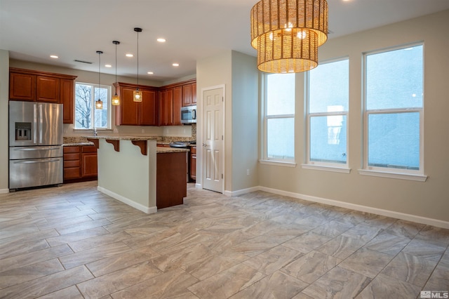 kitchen featuring light stone counters, appliances with stainless steel finishes, a kitchen bar, a center island, and pendant lighting