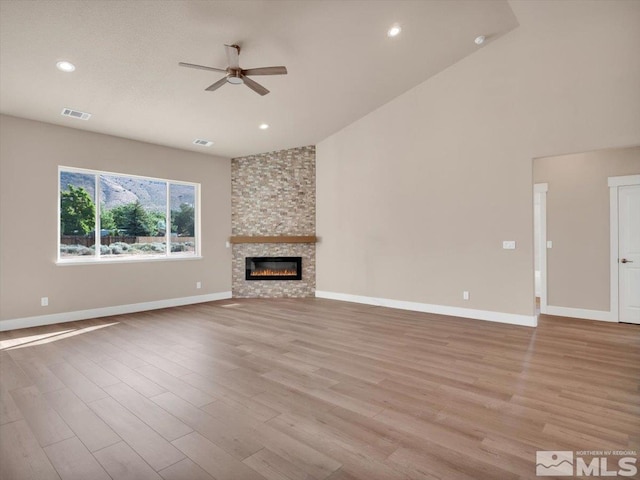 unfurnished living room featuring light wood-type flooring, a stone fireplace, ceiling fan, and lofted ceiling