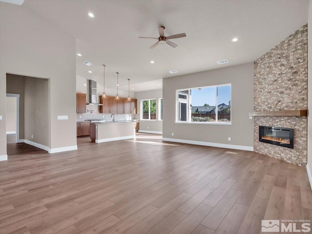 unfurnished living room with a stone fireplace, ceiling fan, sink, and light hardwood / wood-style floors