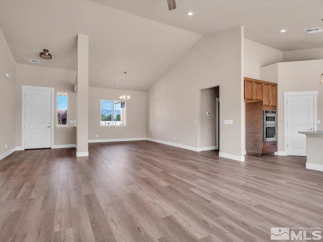 unfurnished living room featuring light hardwood / wood-style flooring, high vaulted ceiling, and a chandelier