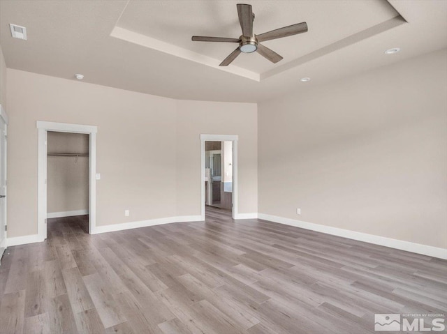 unfurnished bedroom featuring a closet, light hardwood / wood-style flooring, a raised ceiling, and ceiling fan