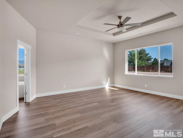 empty room with a tray ceiling, ceiling fan, a textured ceiling, and hardwood / wood-style flooring