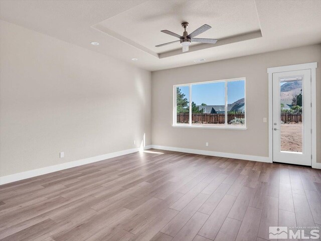 unfurnished room featuring a raised ceiling, a textured ceiling, light hardwood / wood-style flooring, and ceiling fan