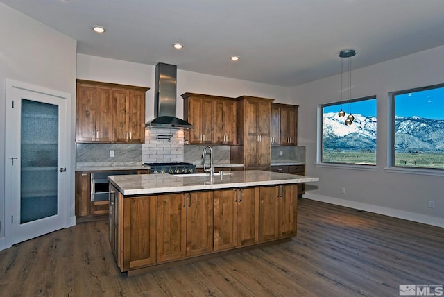 kitchen with decorative light fixtures, sink, a kitchen island with sink, and wall chimney exhaust hood