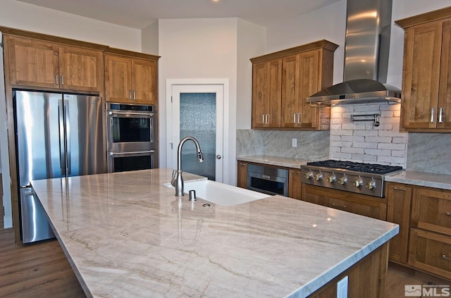 kitchen featuring appliances with stainless steel finishes, tasteful backsplash, an island with sink, sink, and wall chimney exhaust hood