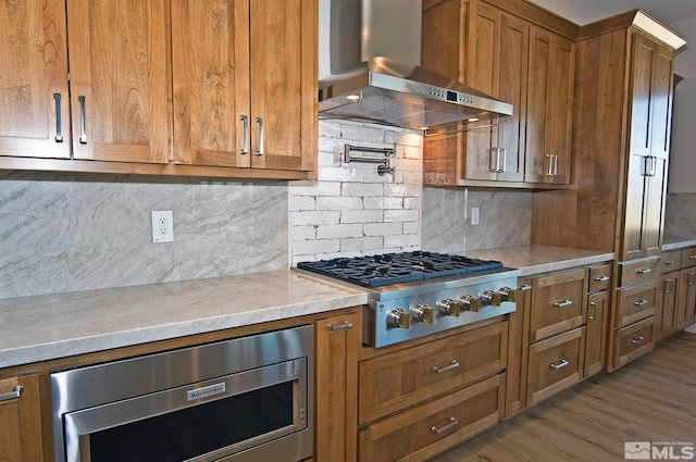 kitchen with ventilation hood, tasteful backsplash, light hardwood / wood-style floors, and stainless steel appliances