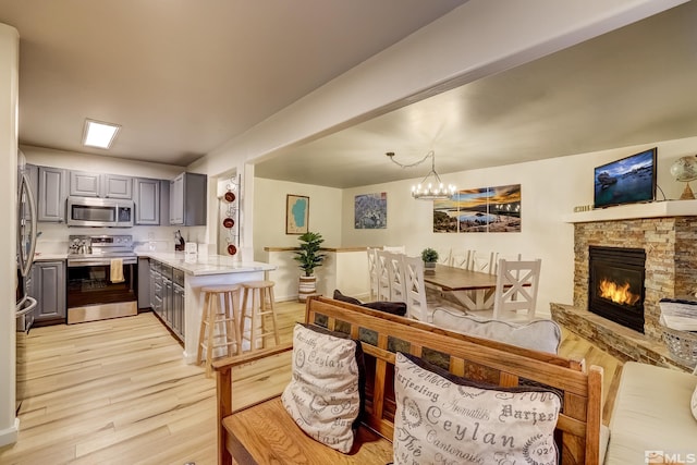 kitchen featuring gray cabinetry, a stone fireplace, appliances with stainless steel finishes, decorative light fixtures, and light hardwood / wood-style floors