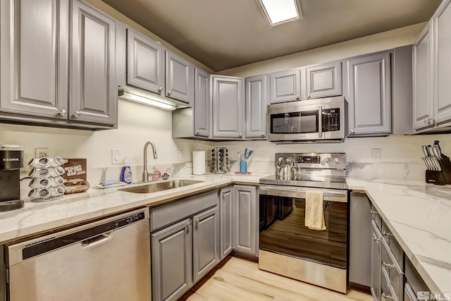 kitchen featuring gray cabinetry, light stone countertops, sink, stainless steel appliances, and light wood-type flooring