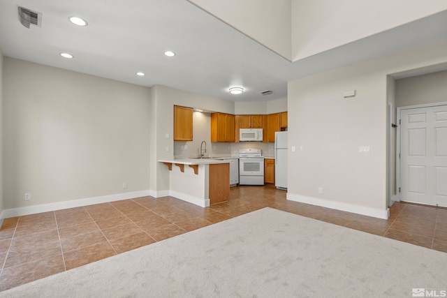 kitchen featuring kitchen peninsula, light carpet, a breakfast bar, white appliances, and sink