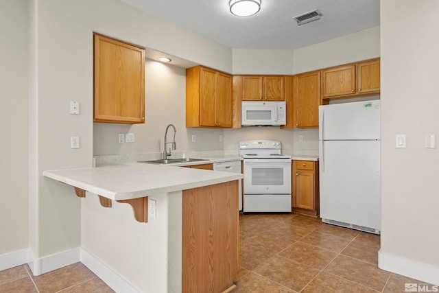 kitchen featuring a breakfast bar, white appliances, sink, light tile patterned floors, and kitchen peninsula