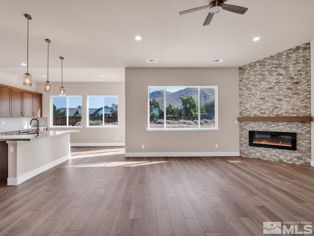 unfurnished living room featuring ceiling fan, light hardwood / wood-style floors, a stone fireplace, and sink