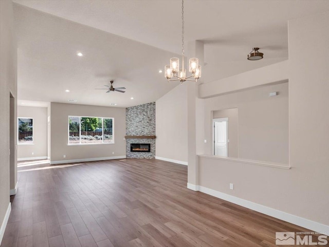 unfurnished living room featuring hardwood / wood-style floors, ceiling fan with notable chandelier, a stone fireplace, and high vaulted ceiling