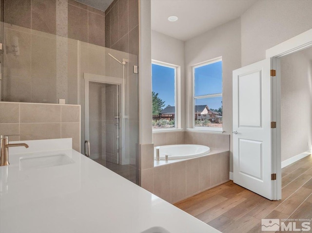 bathroom with hardwood / wood-style flooring, separate shower and tub, and sink