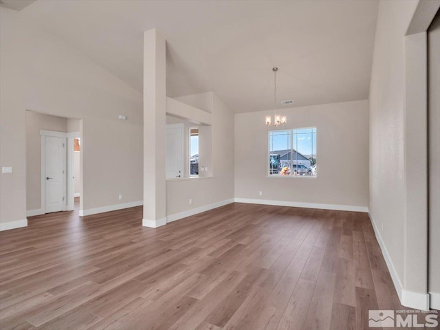 unfurnished dining area with light wood-type flooring, high vaulted ceiling, and an inviting chandelier