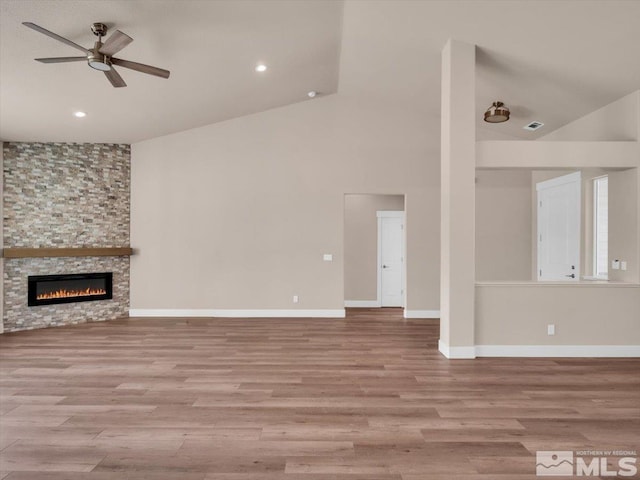 unfurnished living room with high vaulted ceiling, light hardwood / wood-style flooring, ceiling fan, and a stone fireplace