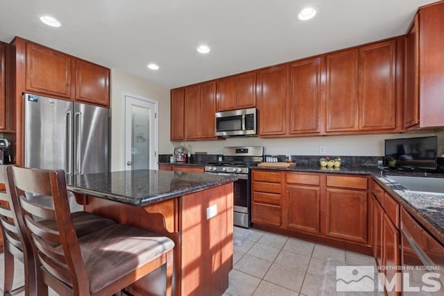 kitchen featuring sink, stainless steel appliances, dark stone counters, a breakfast bar, and light tile patterned floors