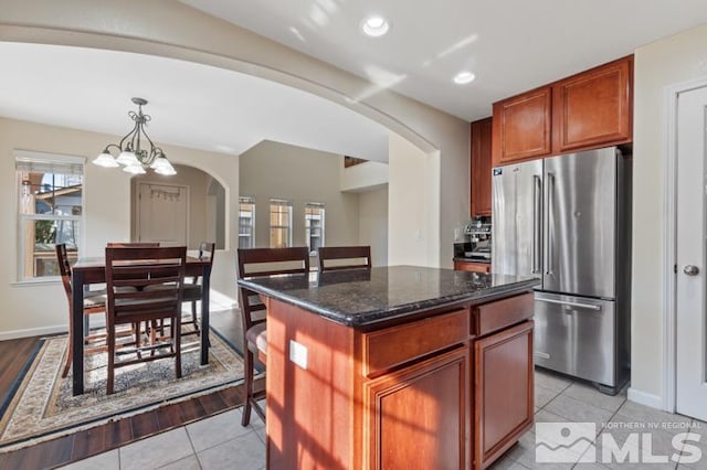 kitchen with pendant lighting, a center island, dark stone counters, light hardwood / wood-style floors, and stainless steel refrigerator