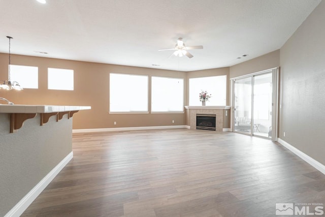 unfurnished living room with hardwood / wood-style flooring, ceiling fan with notable chandelier, and a fireplace