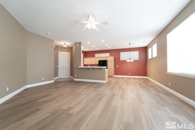 unfurnished living room with ceiling fan with notable chandelier and light hardwood / wood-style flooring