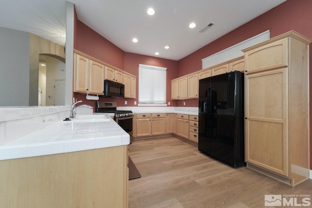 kitchen featuring black appliances, light wood-type flooring, light brown cabinetry, tile counters, and kitchen peninsula