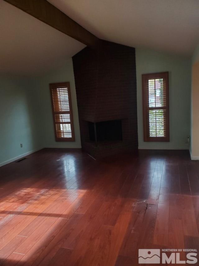 unfurnished living room featuring wood-type flooring, a large fireplace, and lofted ceiling with beams