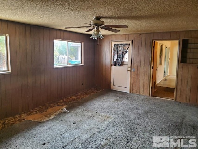 carpeted spare room with a textured ceiling, ceiling fan, and wooden walls