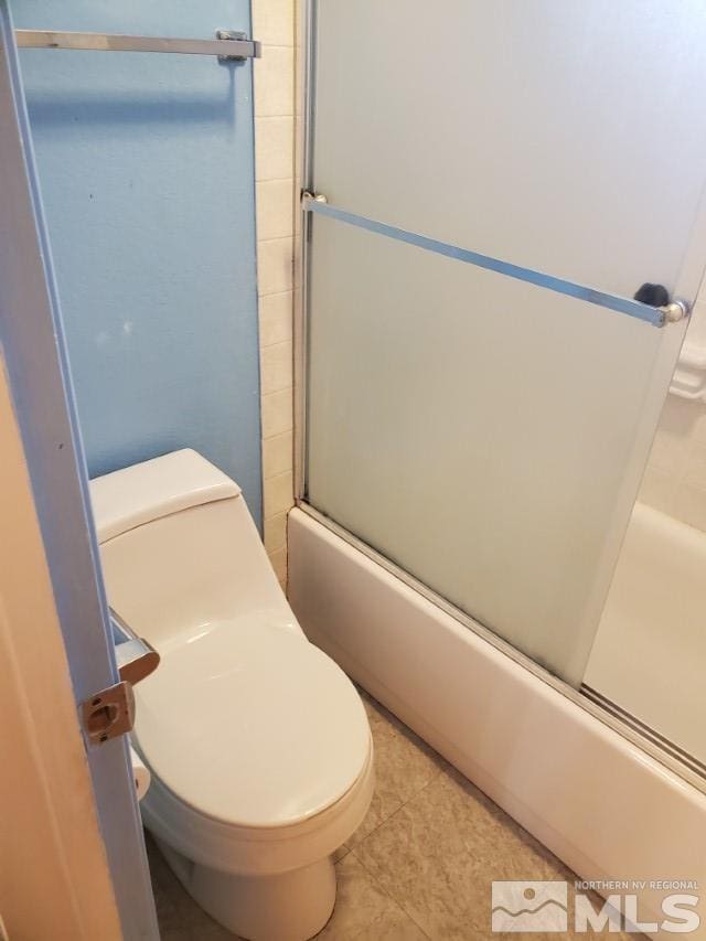 bathroom with tile patterned floors, toilet, and bath / shower combo with glass door