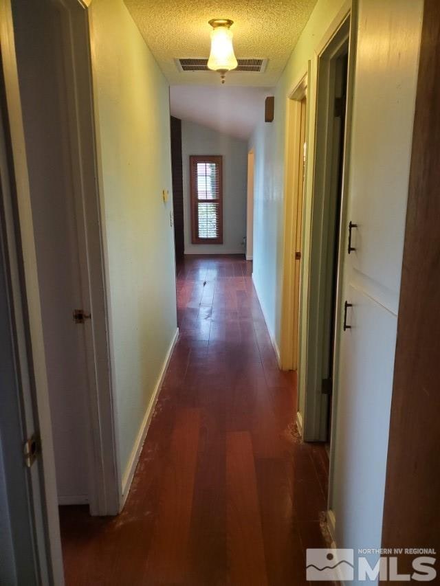 hall with lofted ceiling, a textured ceiling, and dark wood-type flooring