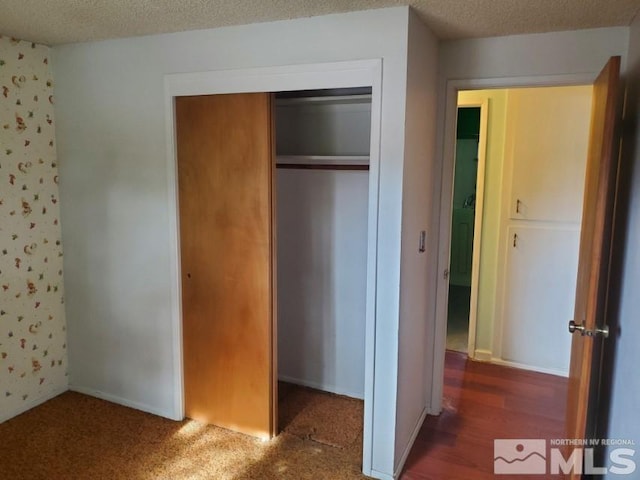 unfurnished bedroom featuring a textured ceiling, a closet, and dark wood-type flooring