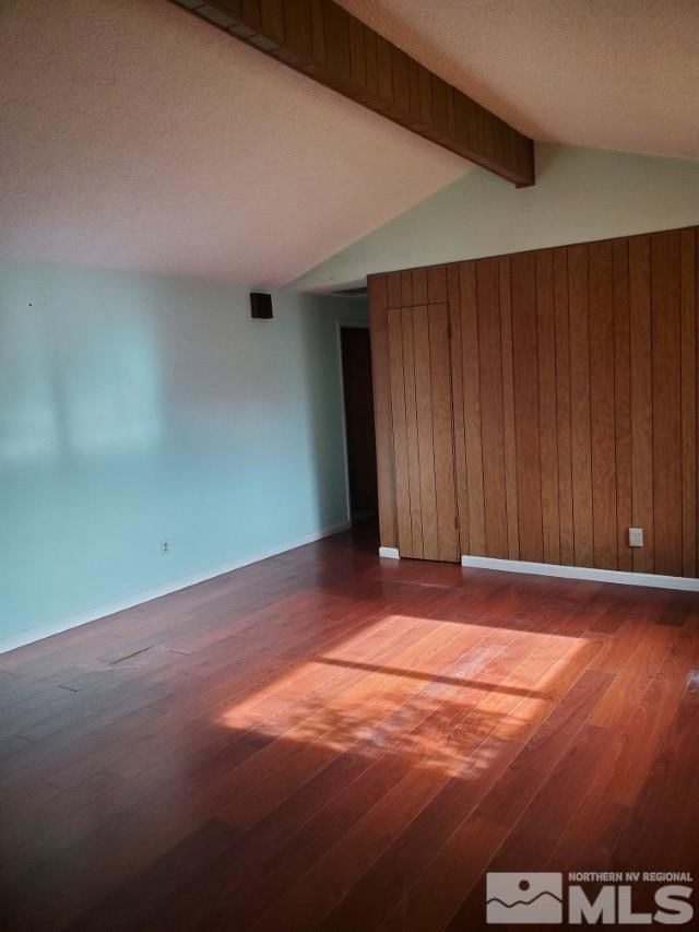 unfurnished room featuring wood-type flooring, vaulted ceiling with beams, a textured ceiling, and wood walls