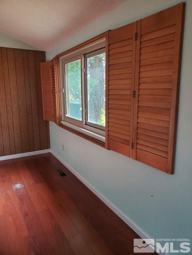 unfurnished room with wood-type flooring, a textured ceiling, and wood walls