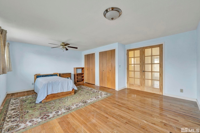 unfurnished bedroom with wood-type flooring, french doors, two closets, and ceiling fan