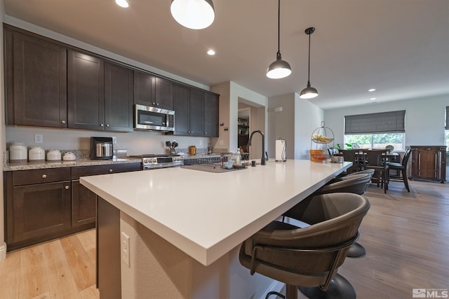 kitchen with light hardwood / wood-style flooring, an island with sink, pendant lighting, and appliances with stainless steel finishes