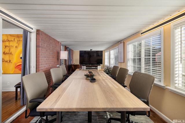 dining room with plenty of natural light, wood-type flooring, and brick wall