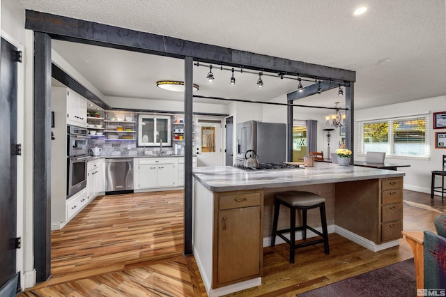 kitchen with track lighting, white cabinets, light stone countertops, a textured ceiling, and stainless steel appliances